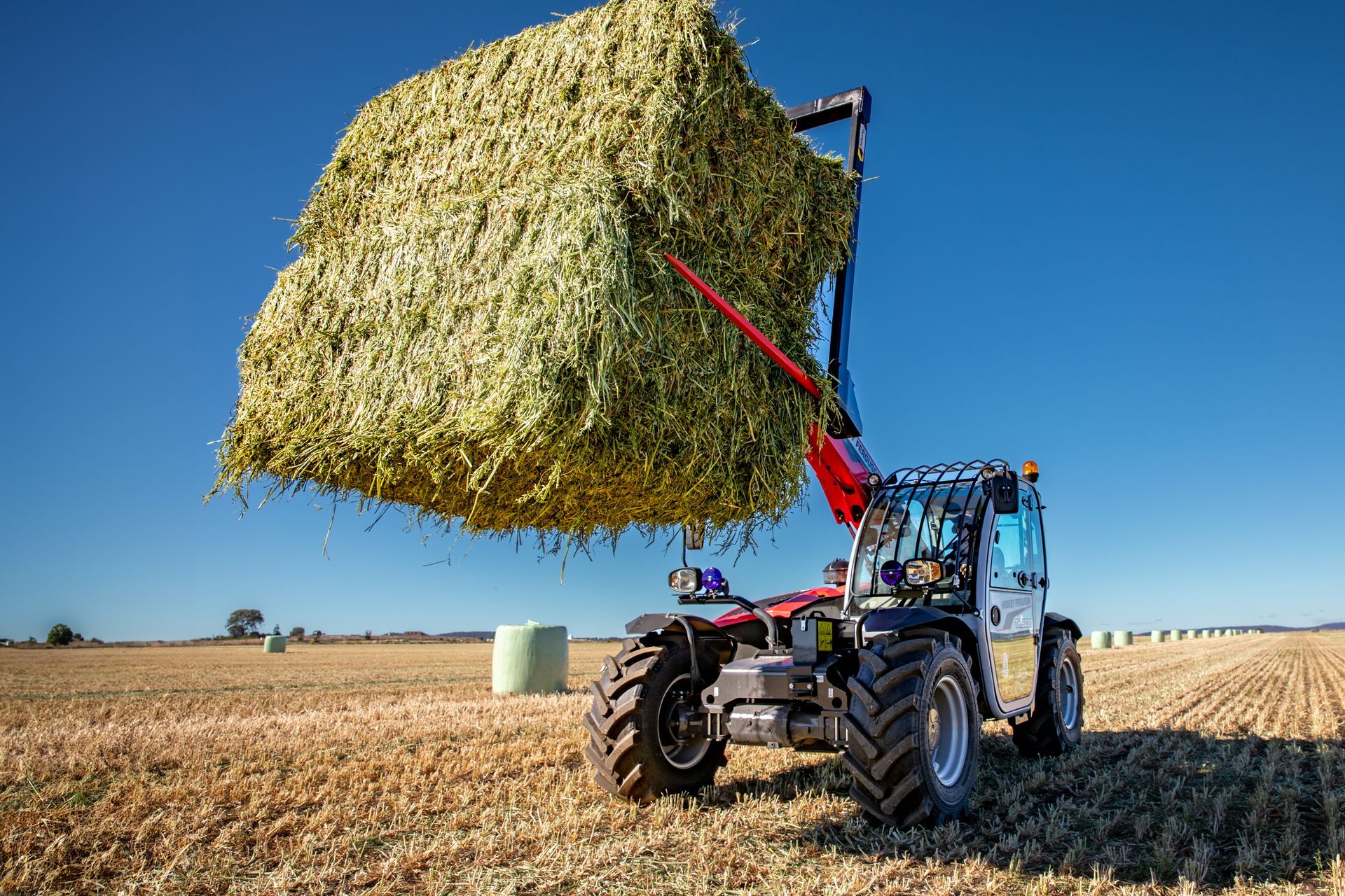 A red tractor is pulling a trailer full of hay bales.