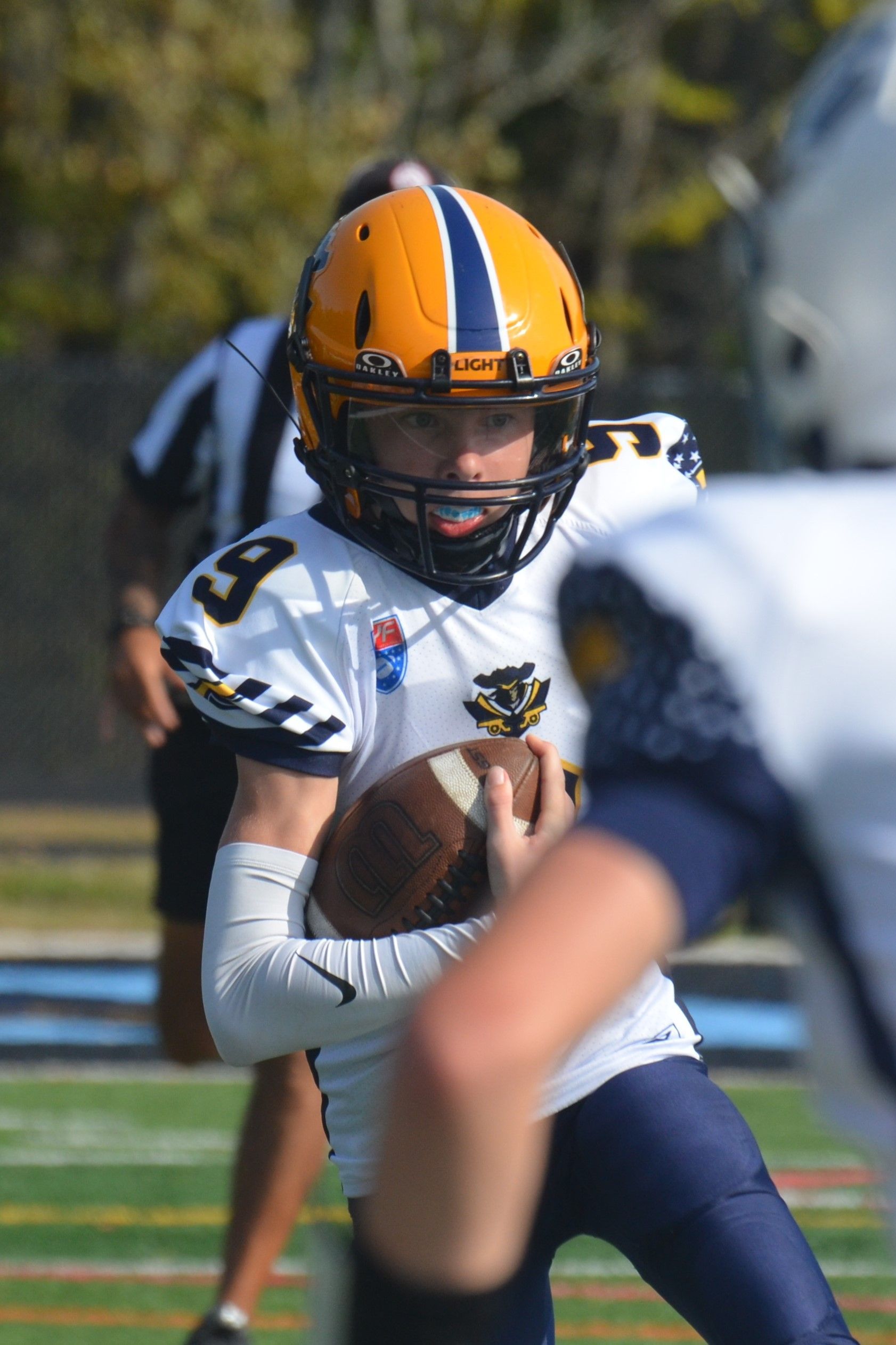Football player in maroon jersey holding ball, smiling, surrounded by teammates on a field.
