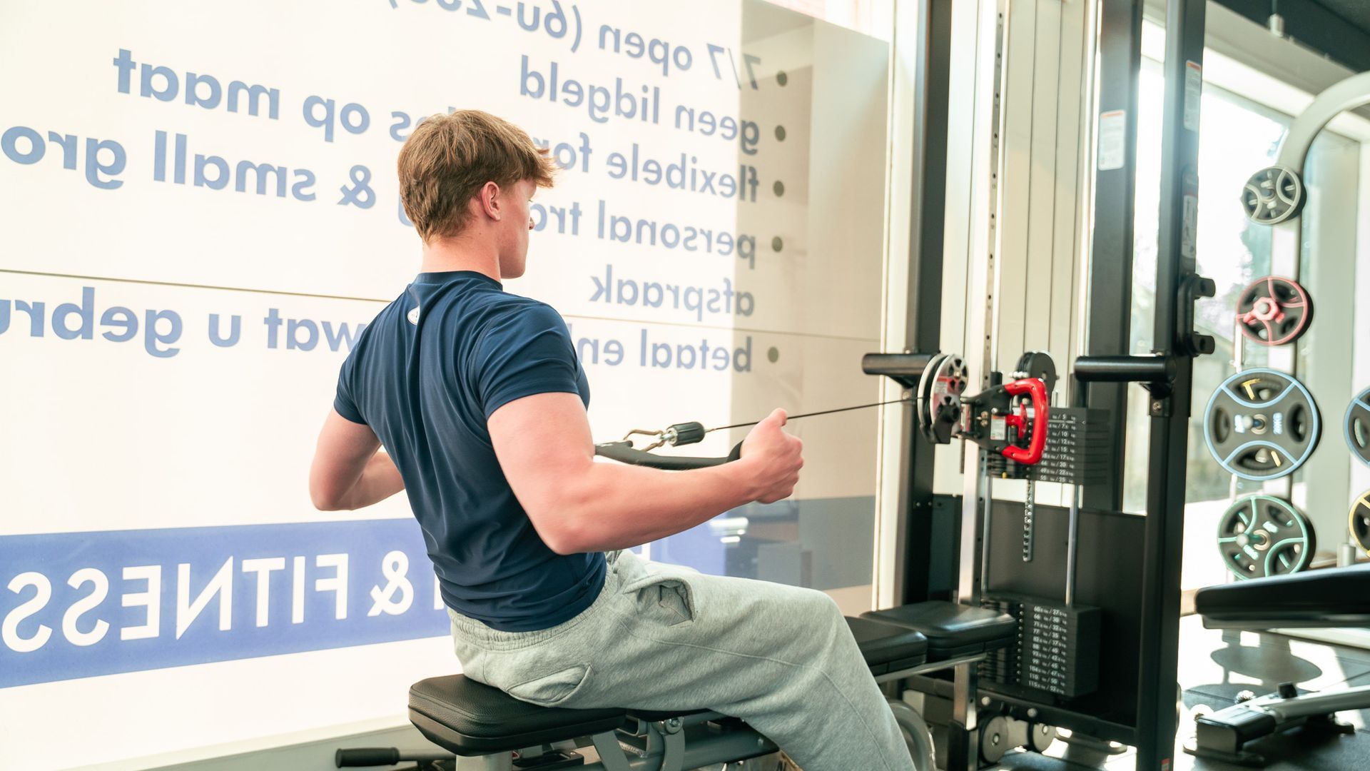 Een man zit op een roeimachine in een sportschool.