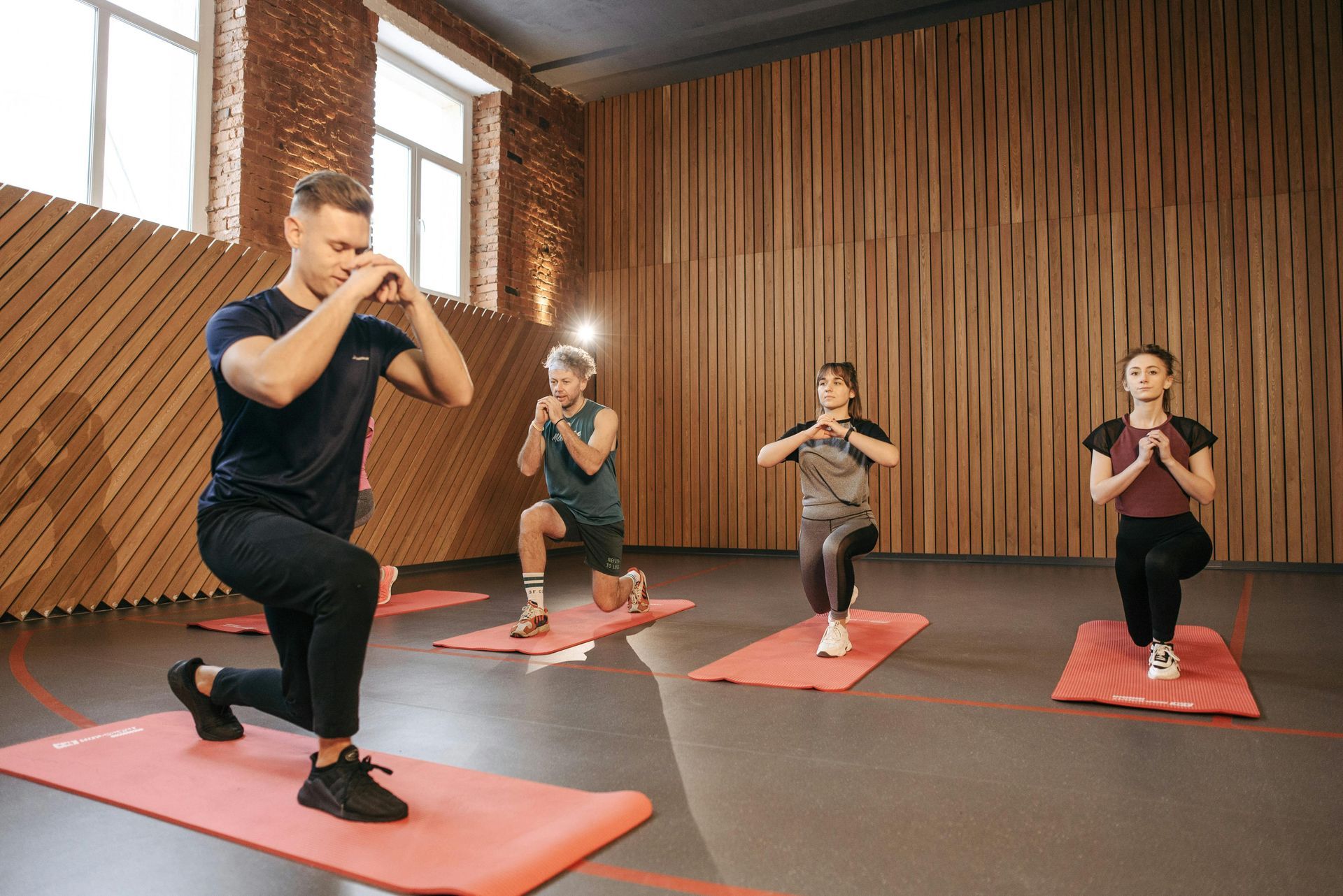 People doing lunges on mats in a wooden-walled gym.