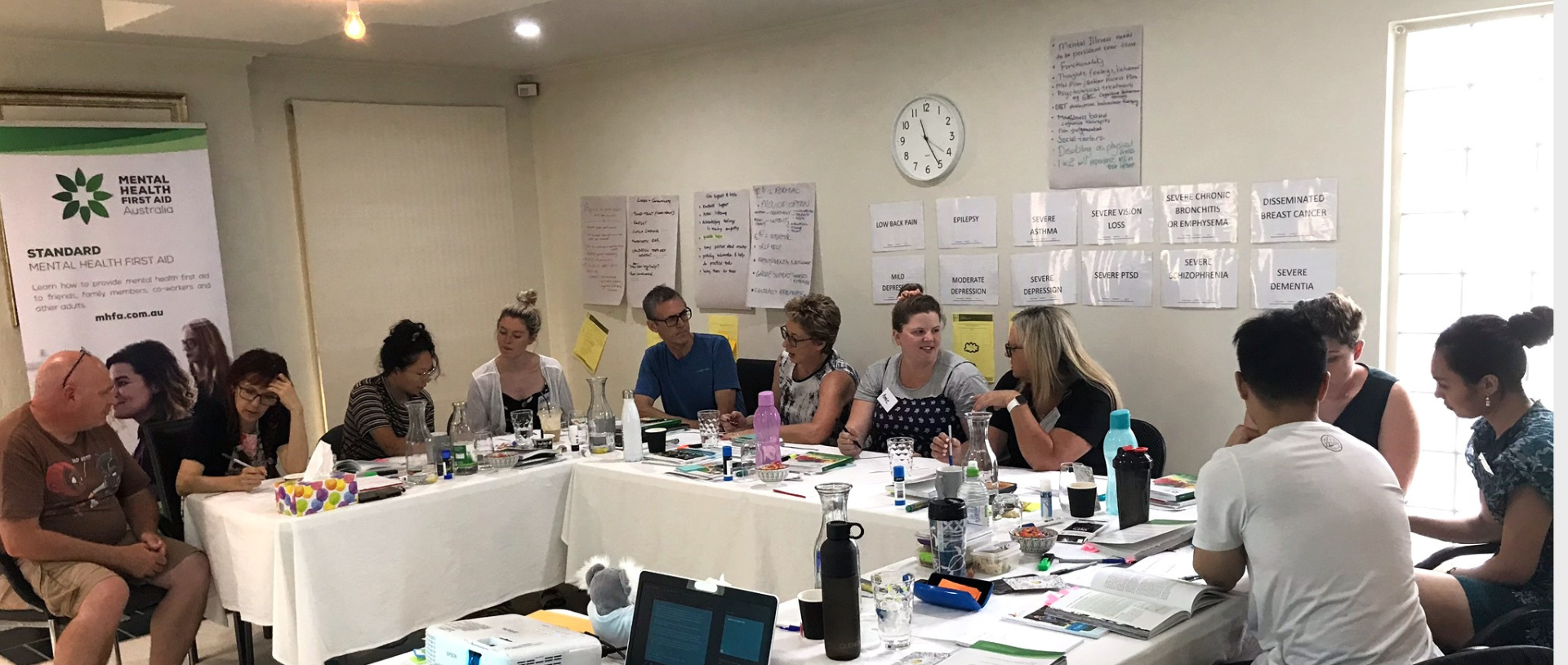 People sitting around a table in a meeting, with posters on the wall and various objects on the table.
