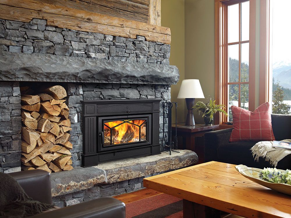 A fireplace with a wood stove in it is sitting in a living room next to a rug.