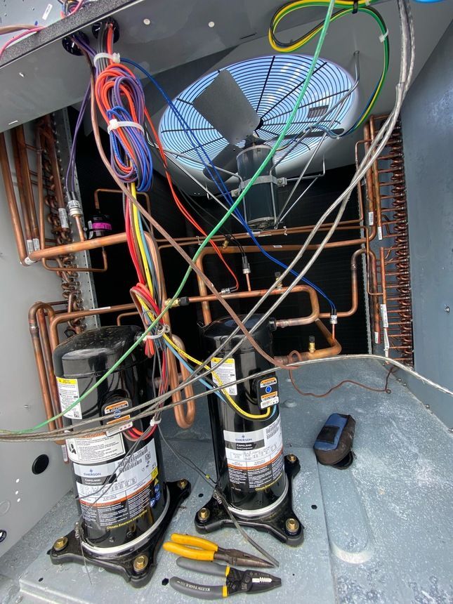 HVAC unit with two black compressors, copper tubing, wires, and tools.