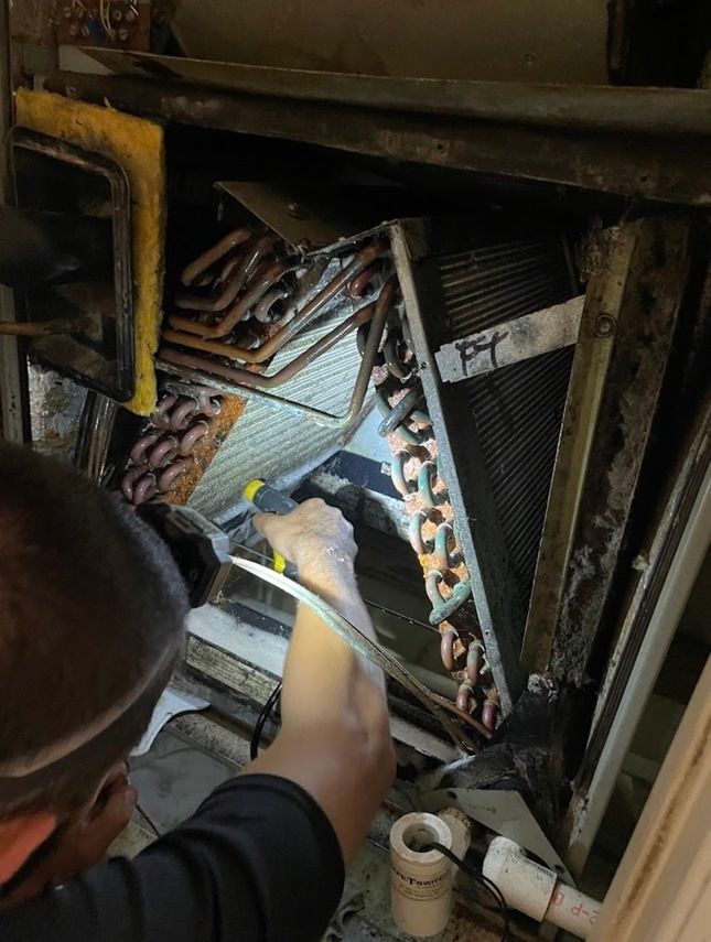 A person examining HVAC coils with a flashlight. Inside equipment, copper tubes visible, some insulation.