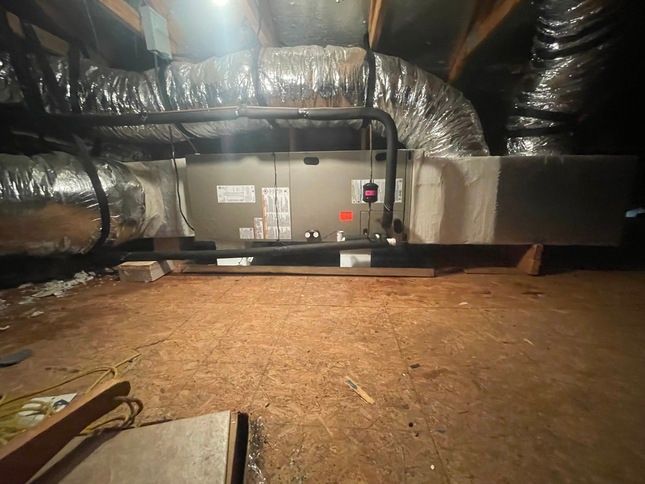 HVAC unit in an attic with ductwork. Wooden floor and insulation visible.