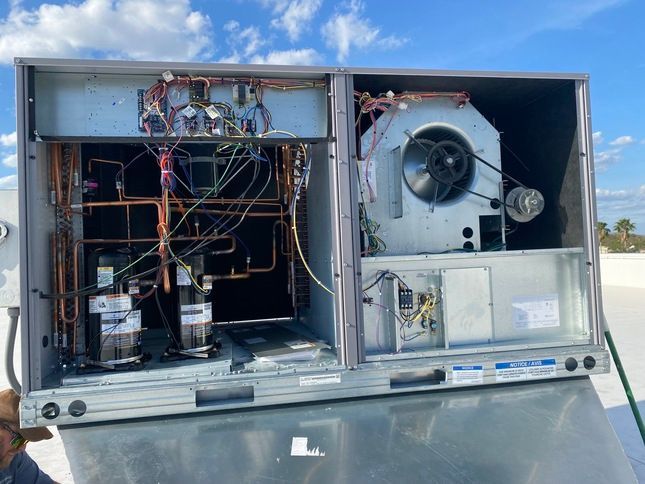 Opened HVAC unit on a rooftop, revealing internal components and wiring.