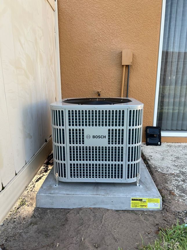 Bosch air conditioning unit on a concrete pad next to a stucco wall and a fence.