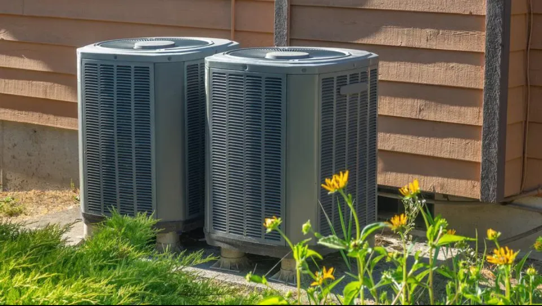 Two air conditioners are sitting outside of a house.