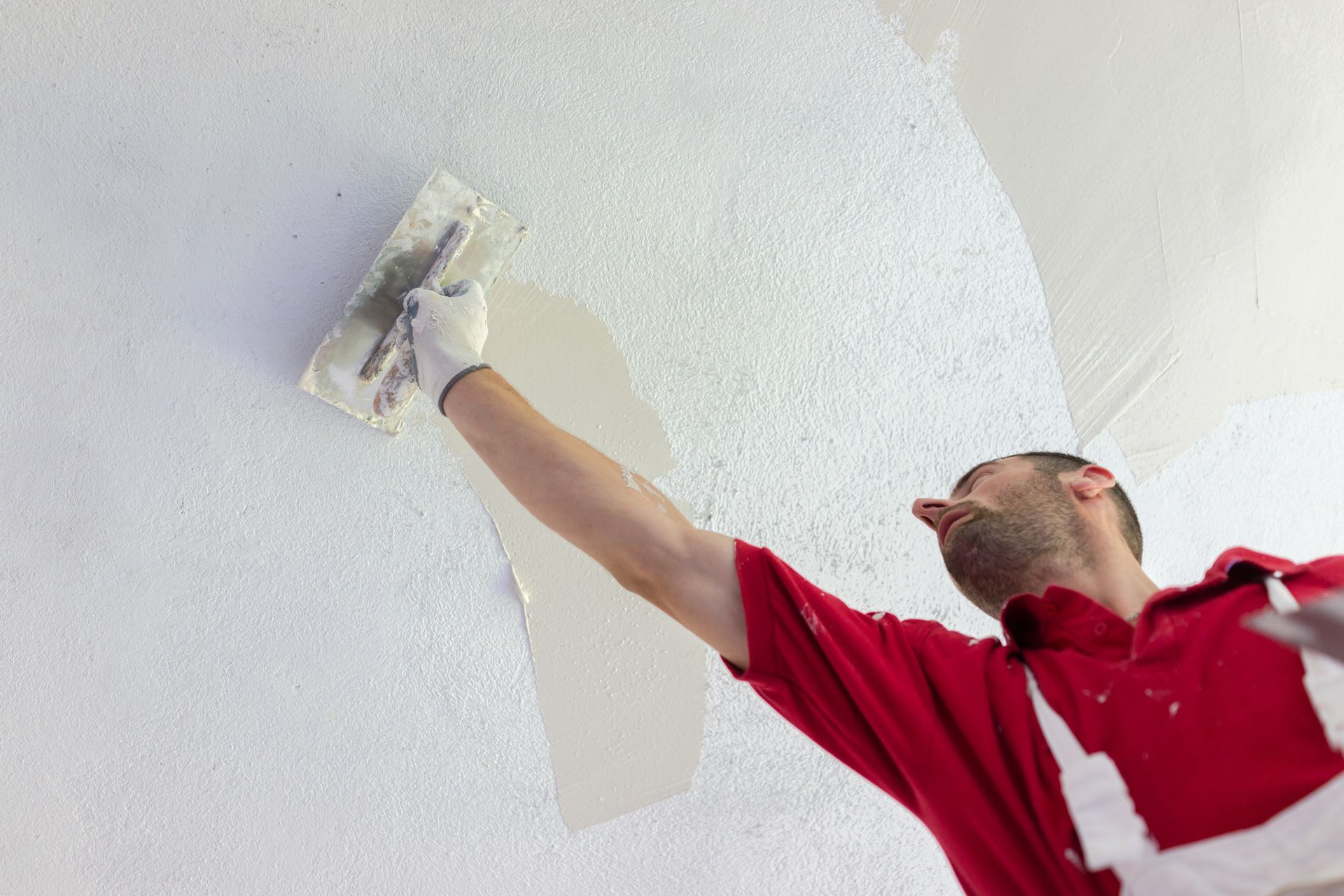 A man in a red shirt is plastering a wall with a trowel.