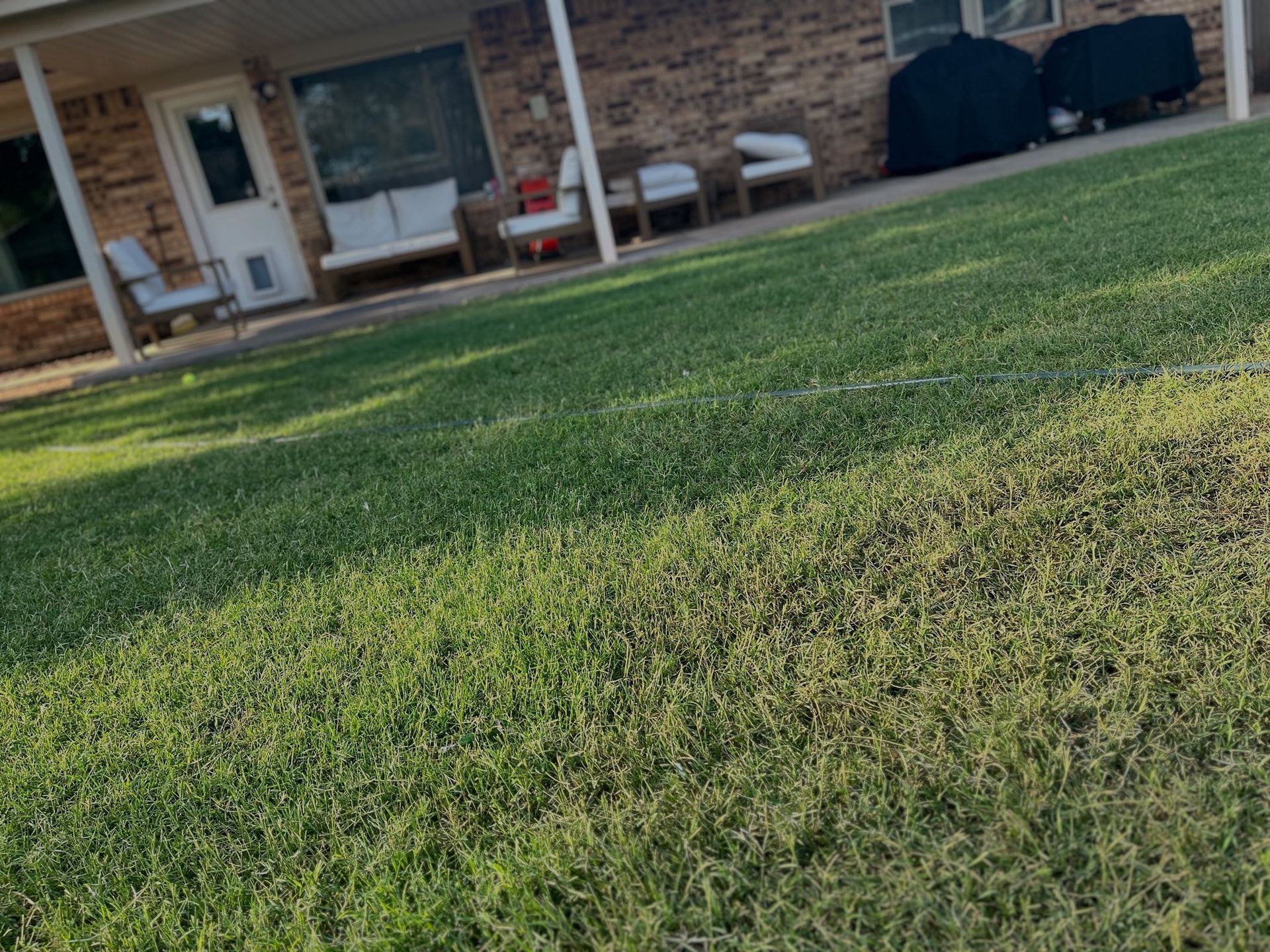 Green lawn in front of a brick house with patio furniture.