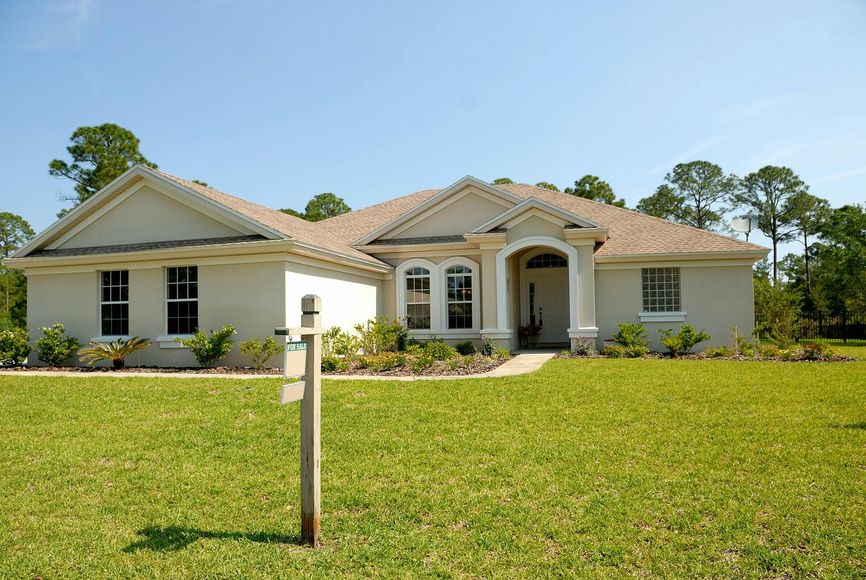 A beige, one-story house on a grassy lawn with a