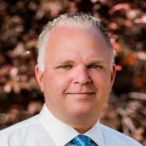 A man in a white shirt and blue tie is smiling for the camera.