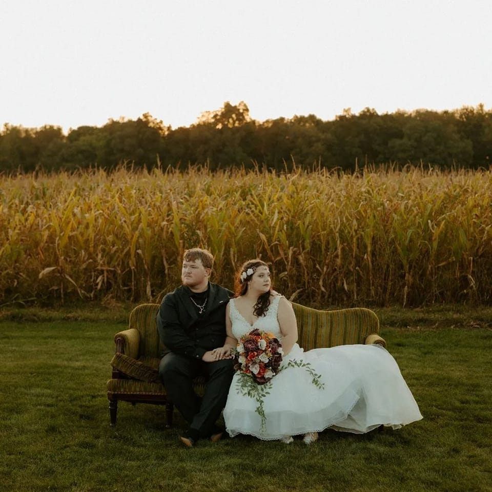 a bride and groom are sitting on a couch in a field .