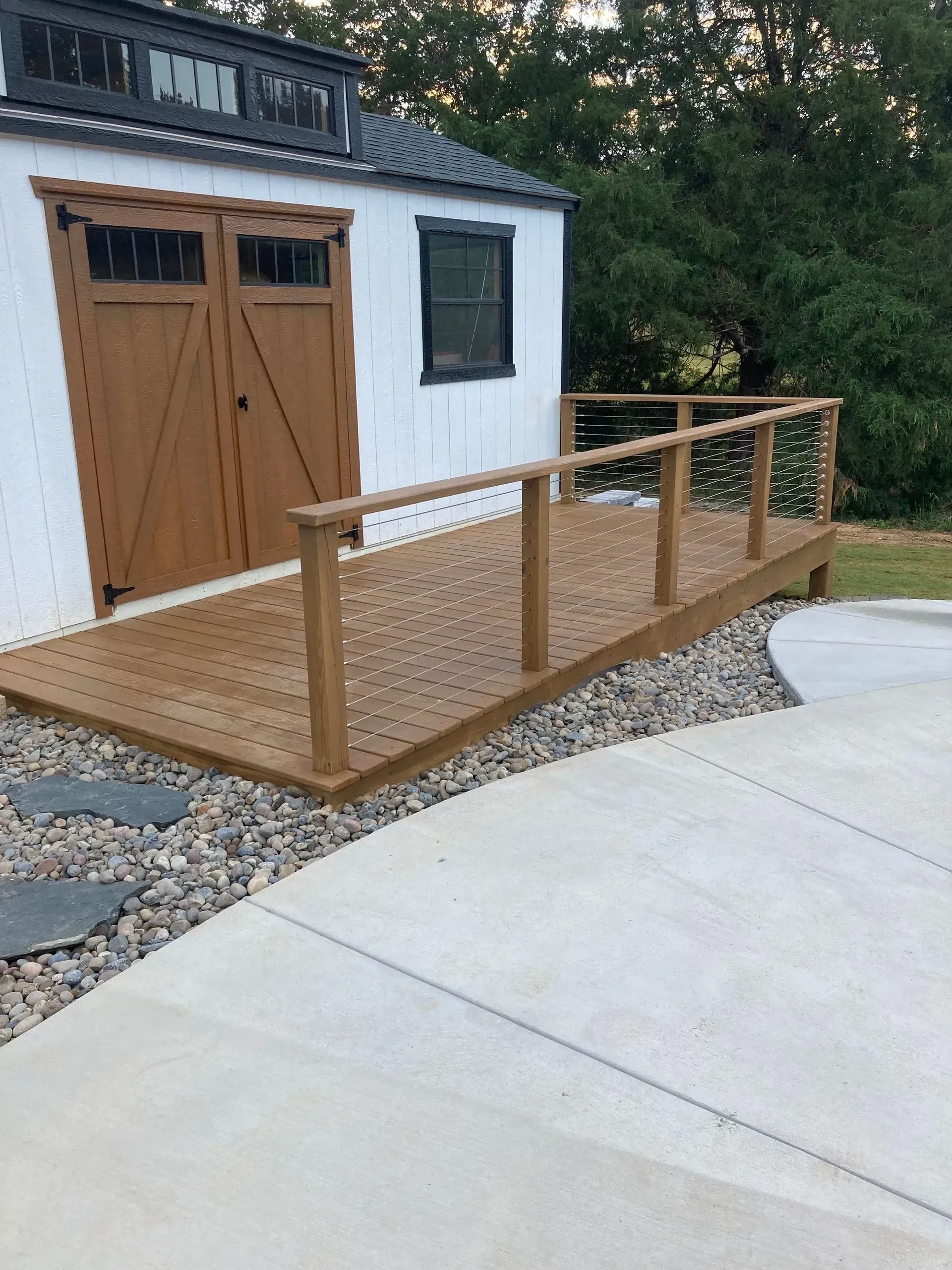 Wooden deck with railing and ramp access to a white building with brown doors.