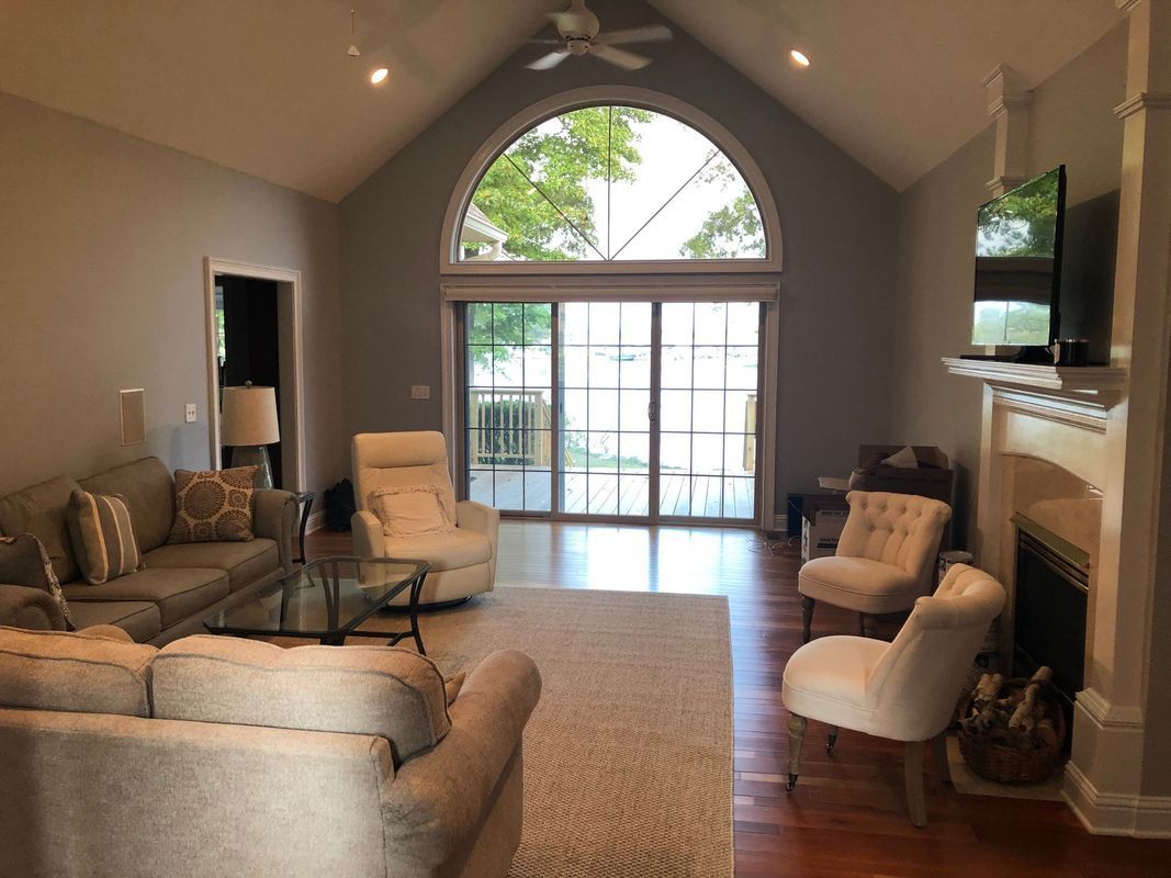 Living room with high ceiling, arched window, fireplace, couch, chairs, and sliding glass doors.