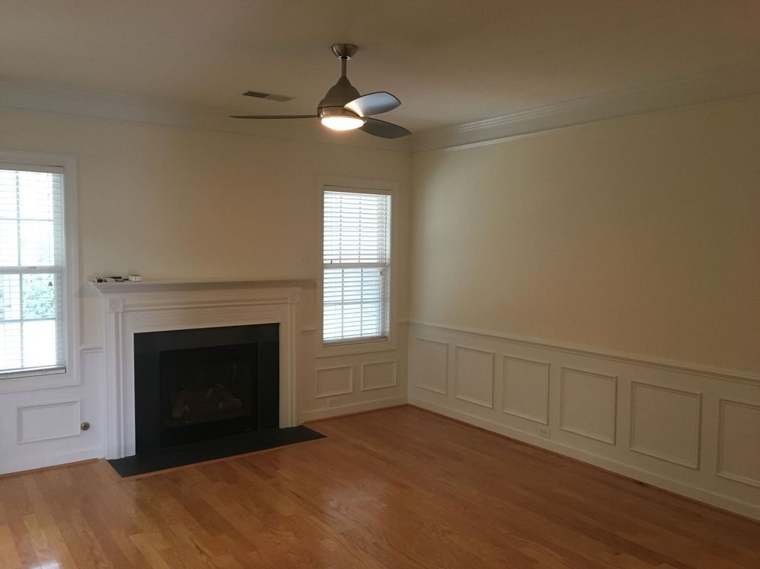 Empty living room with fireplace, windows, hardwood floors, and a ceiling fan.