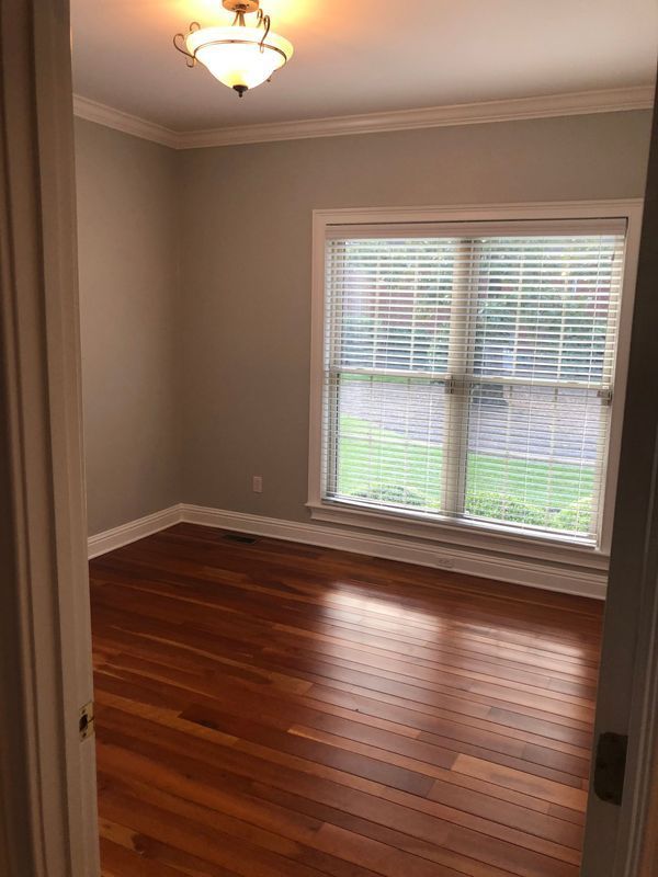 Empty room with hardwood floors, a window with blinds, and a light fixture.