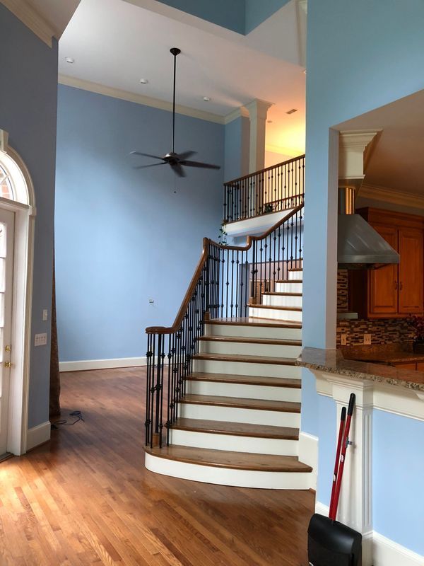 A staircase with wood steps and black iron railings in a home with light blue walls and hardwood floors.