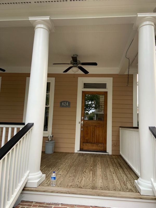 Porch of a house with white columns, brown door, and a ceiling fan.