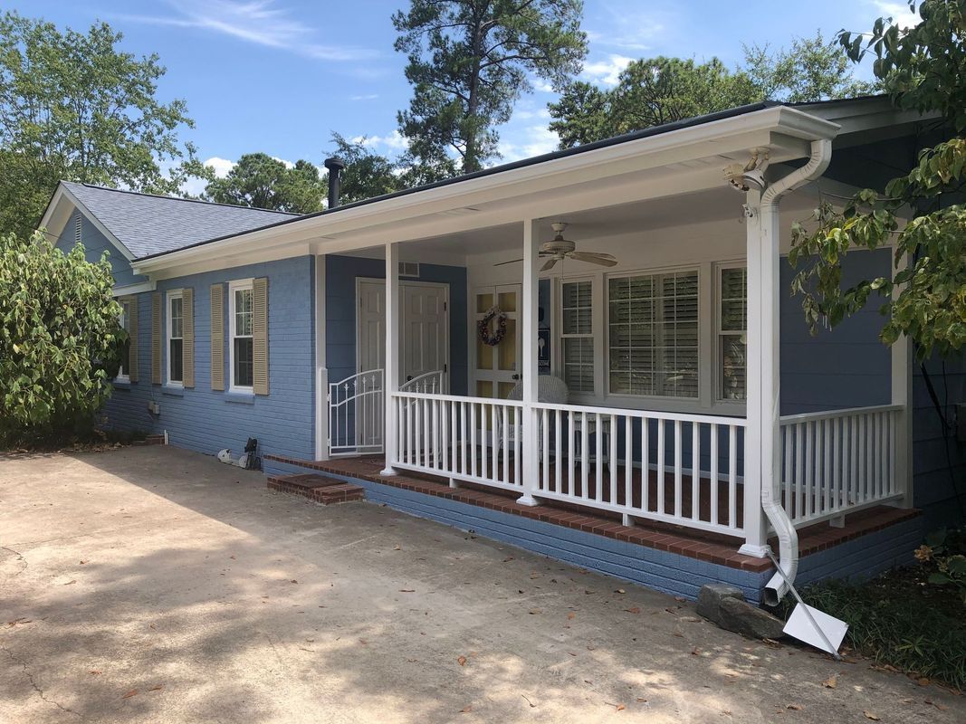 Blue house with a white porch and railing, surrounded by trees.