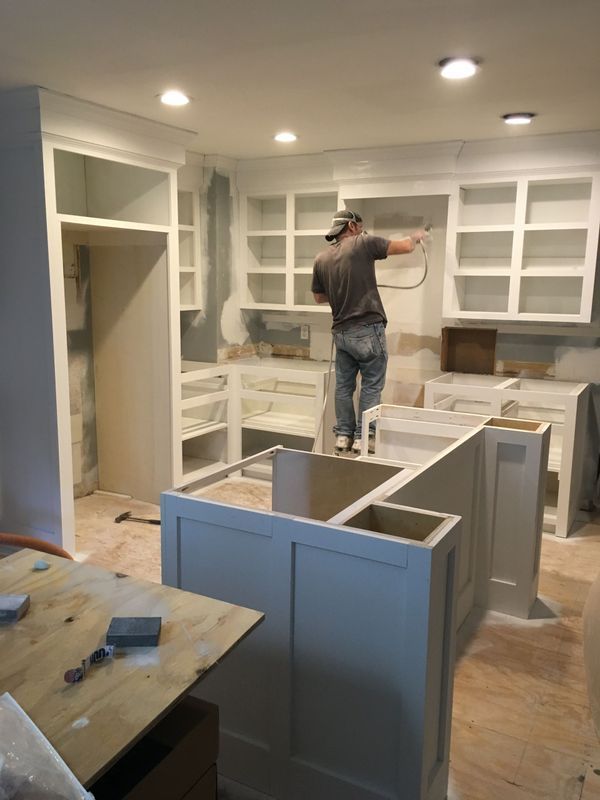 Person spraying paint in a partially constructed kitchen, cabinets and island, interior view.