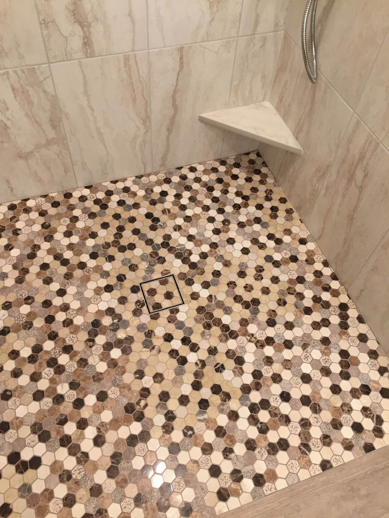 A shower stall with a tiled floor and a corner shelf.