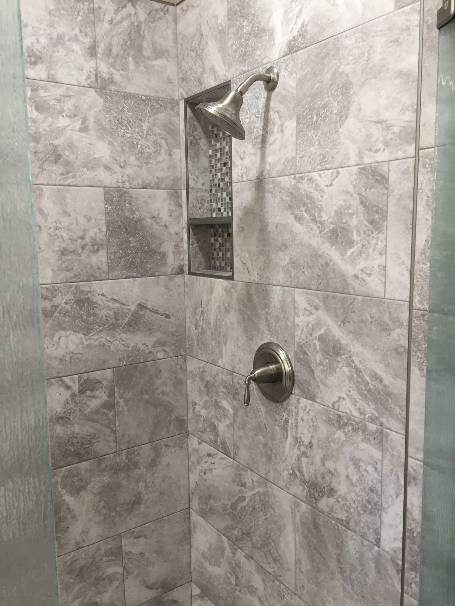 A shower with gray tiles and a stainless steel shower head.
