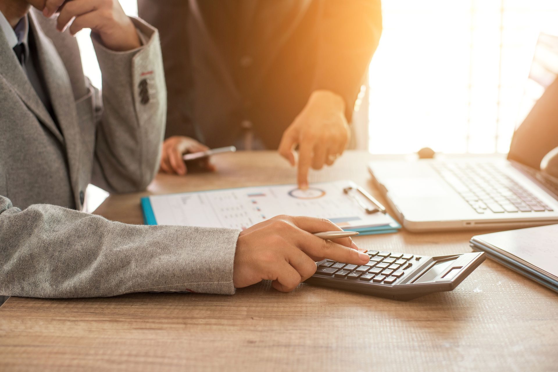 Two professionals reviewing charts and using calculator at desk in office for financial analysis.