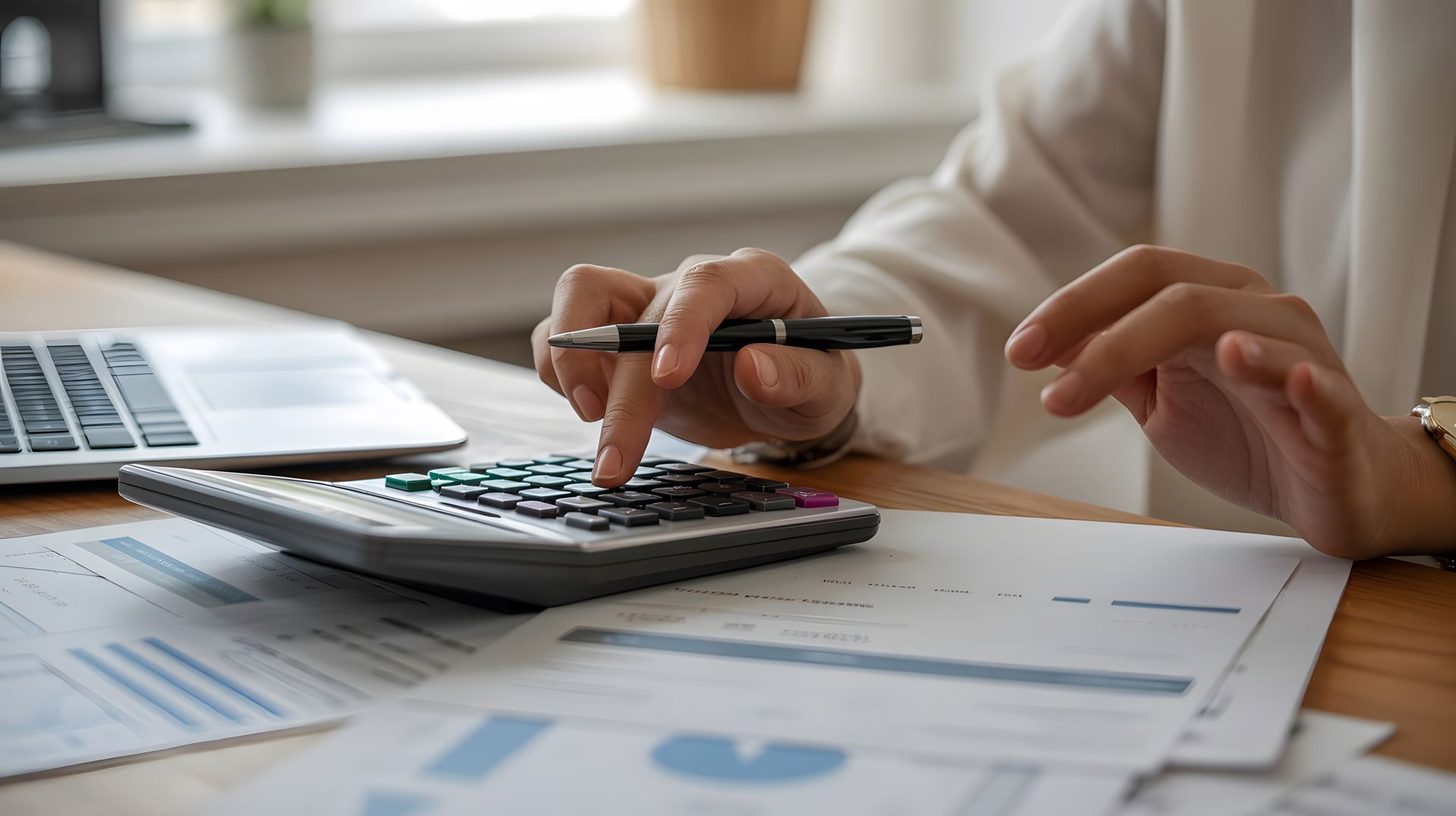 Person using a calculator with a pen, reviewing documents, likely in an office setting. Person using a calculator with a pen, reviewing documents, likely in an office setting.