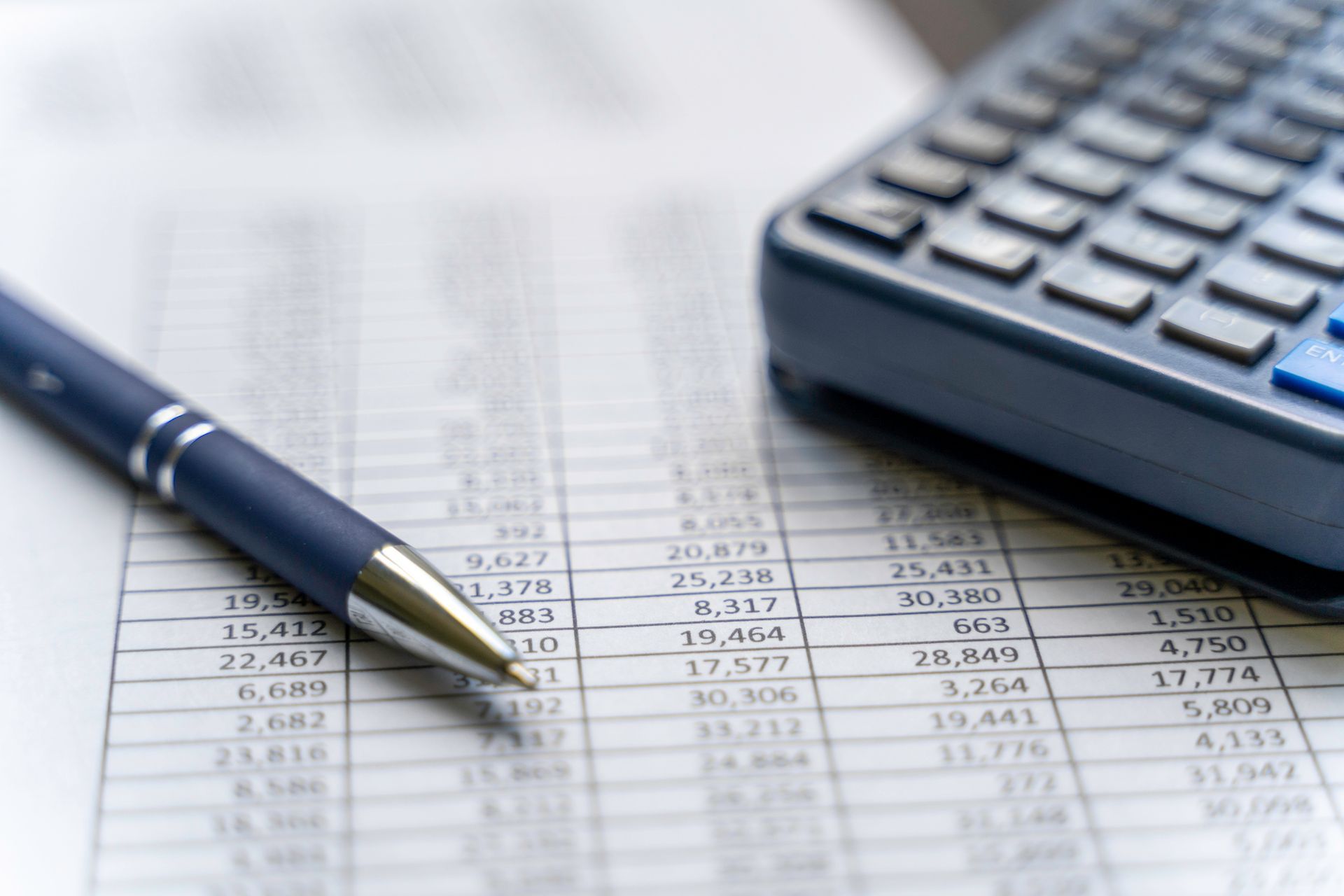 Pen and calculator resting on financial spreadsheet filled with rows of accounting data.