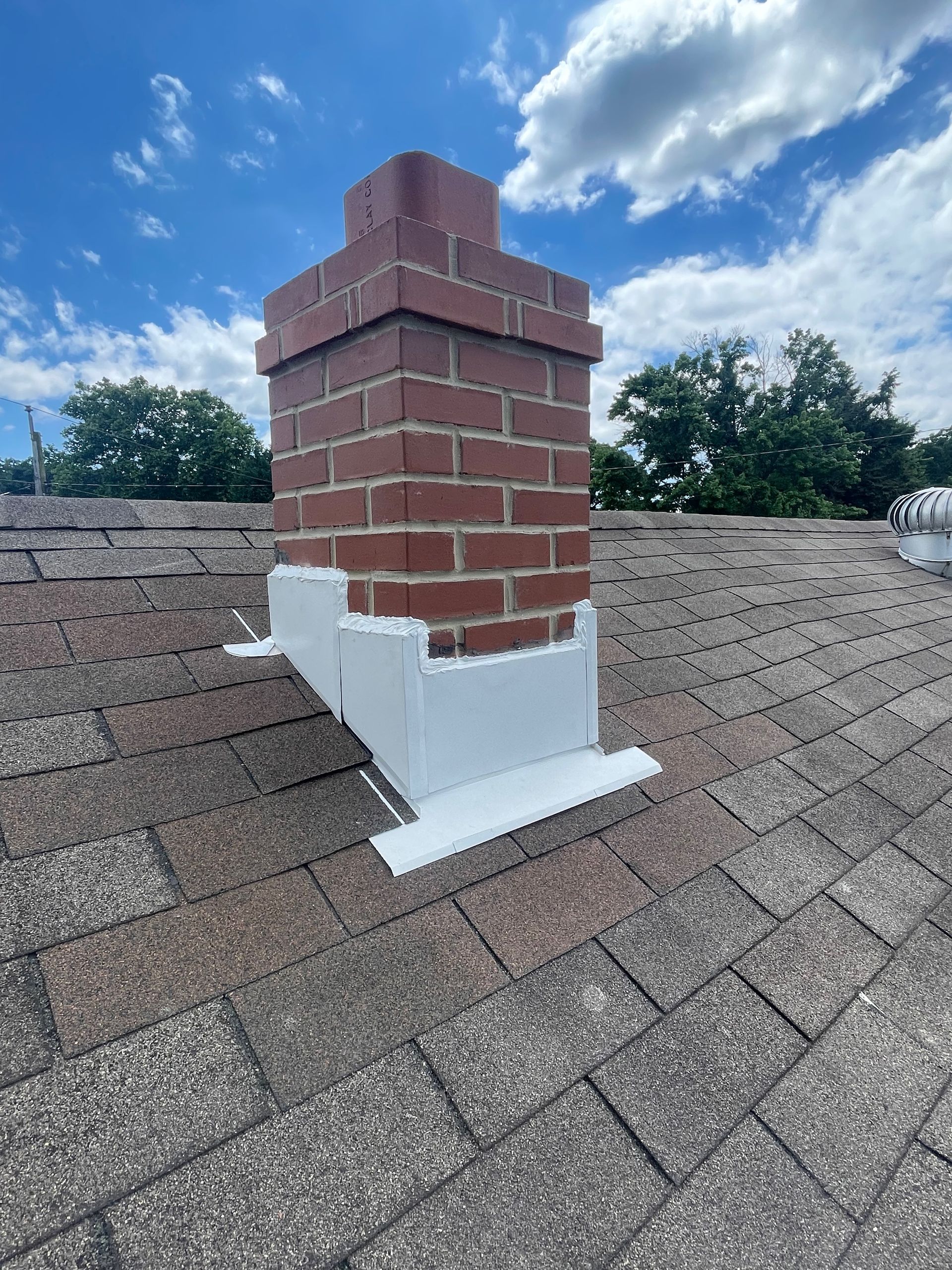 A brick chimney is sitting on top of a roof. rebuilt and flashed middleriver omni-roof.com