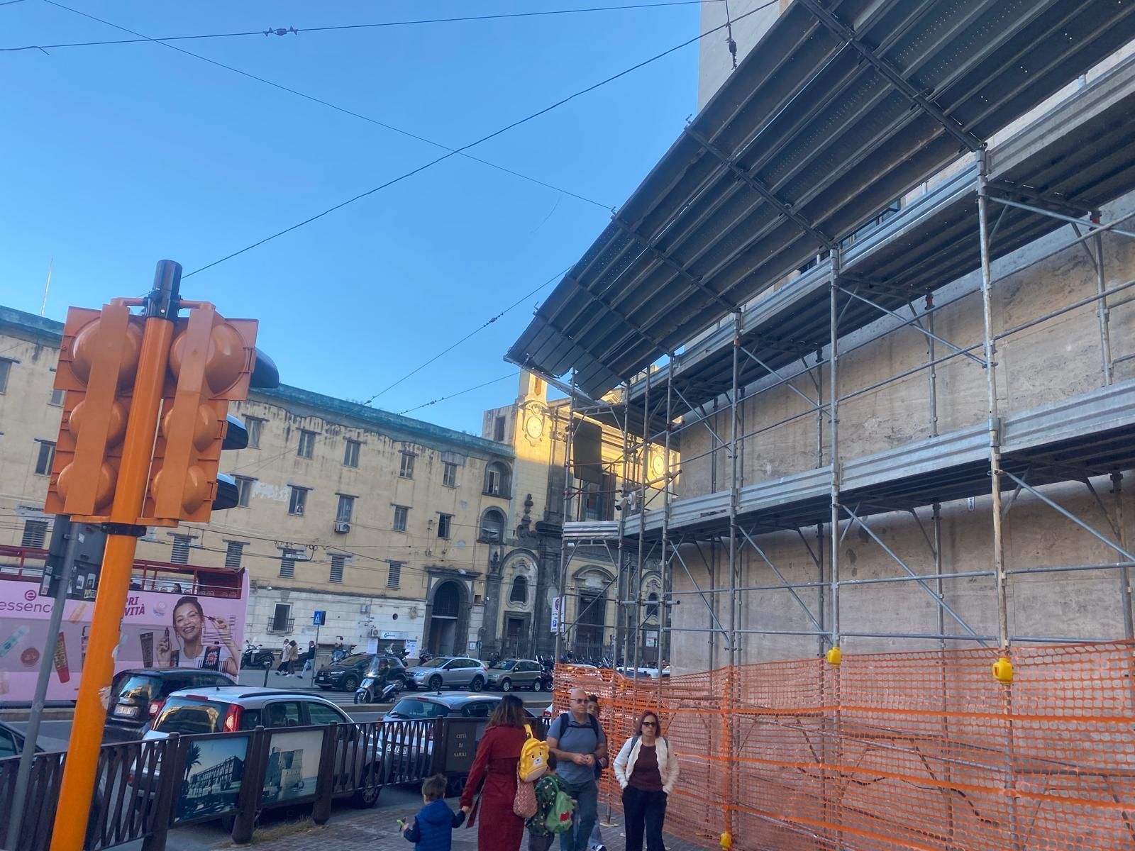 Scena di strada con edifici, impalcature, persone e semaforo.