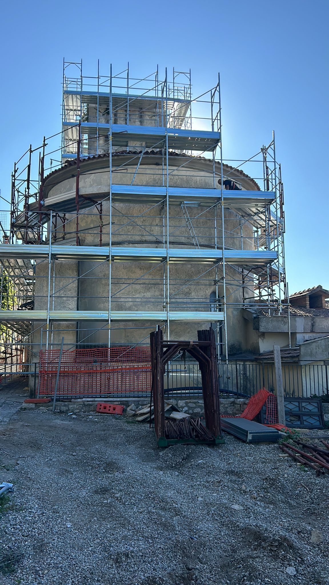 Un'impalcatura circonda un edificio rotondo in mattoni in costruzione, che si staglia contro un cielo azzurro e terso.
