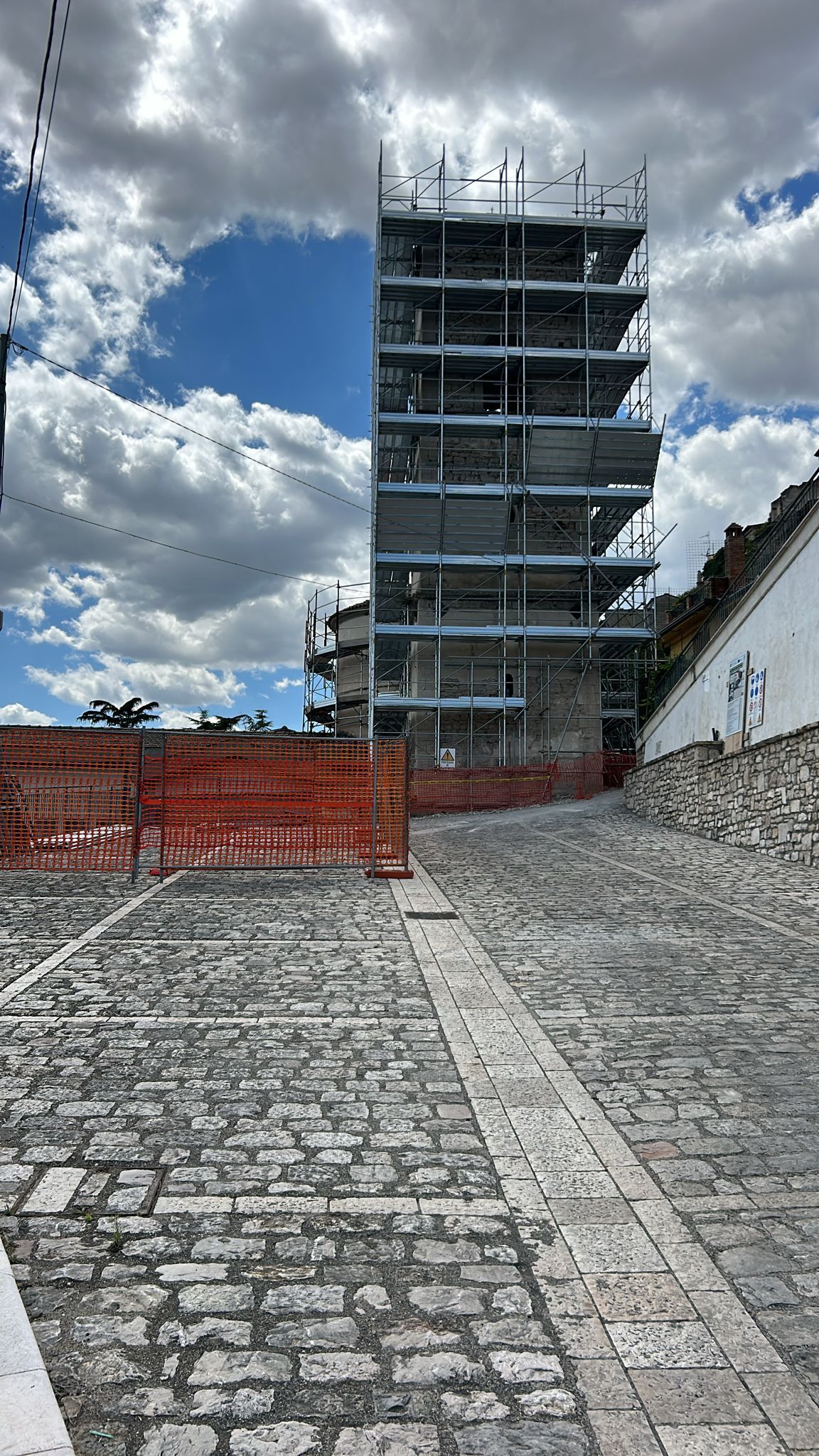 Un'impalcatura circonda un alto edificio su una strada acciottolata, con il cielo luminoso sopra.