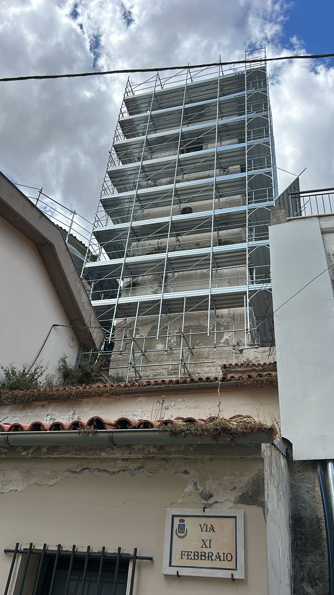 La struttura dell'edificio in costruzione si erge sopra i tetti, contro un cielo nuvoloso.