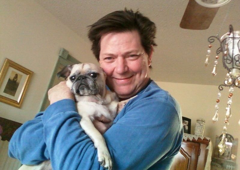 A man in a blue shirt is holding a pug dog