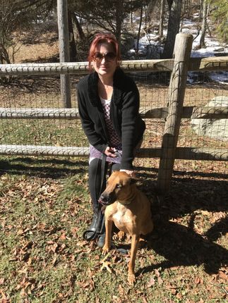A woman is sitting next to a dog in front of a wooden fence.