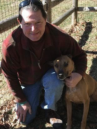 A man is kneeling down next to a brown dog.