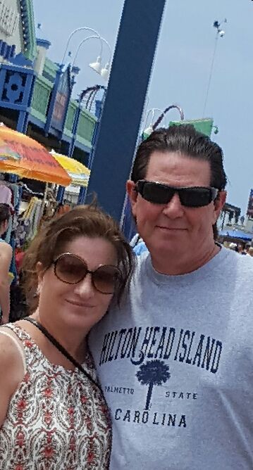A man and a woman are posing for a picture . the man is wearing a shirt that says cotton head island.