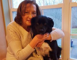 A woman is holding a black dog in her arms in front of a window.