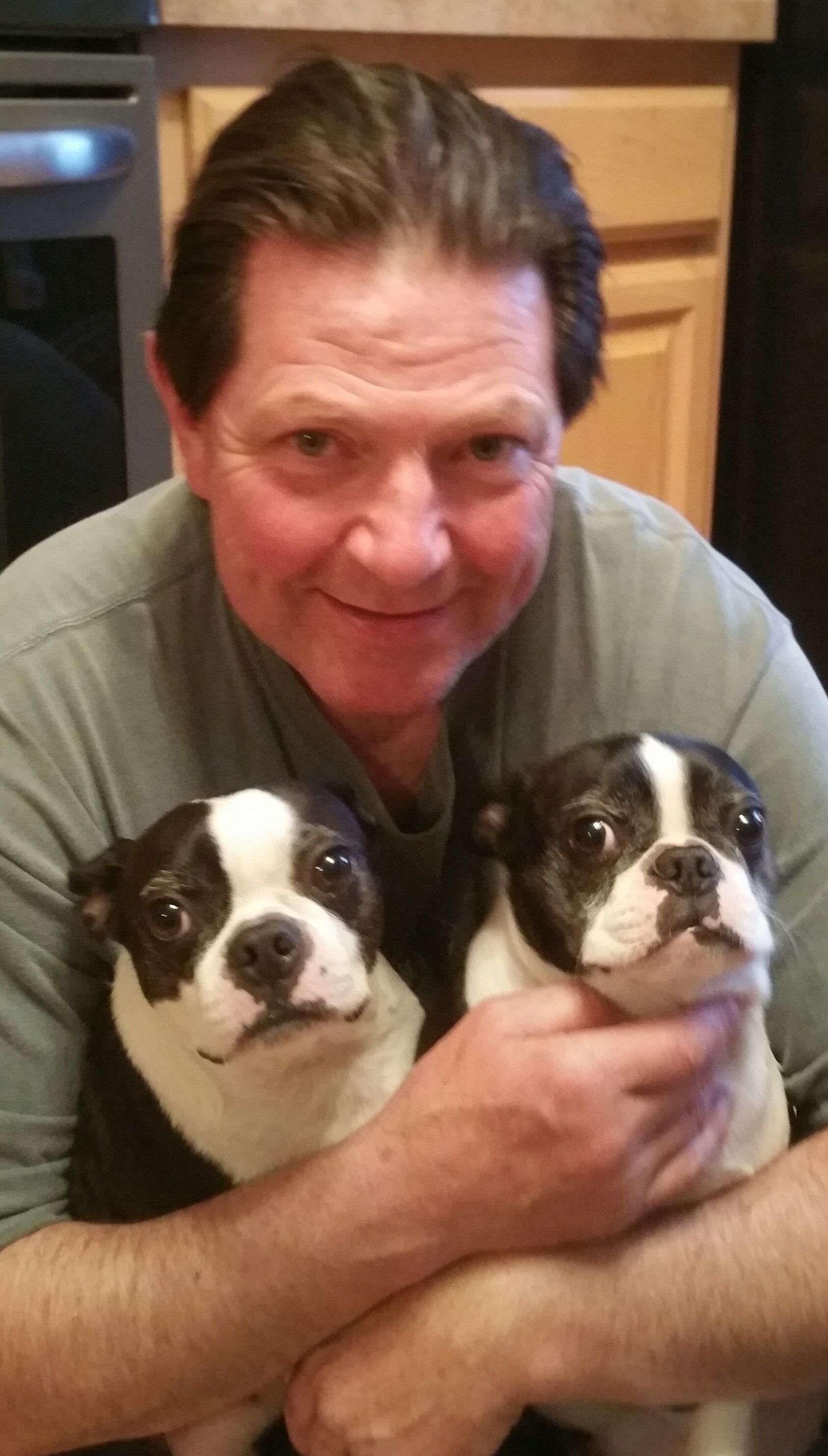 A man is holding two boston terrier puppies in his arms