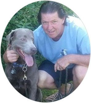 A man in a blue shirt is kneeling down next to a dog