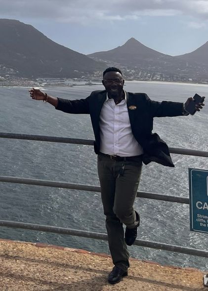 A man in a suit is standing on a ledge overlooking the ocean.