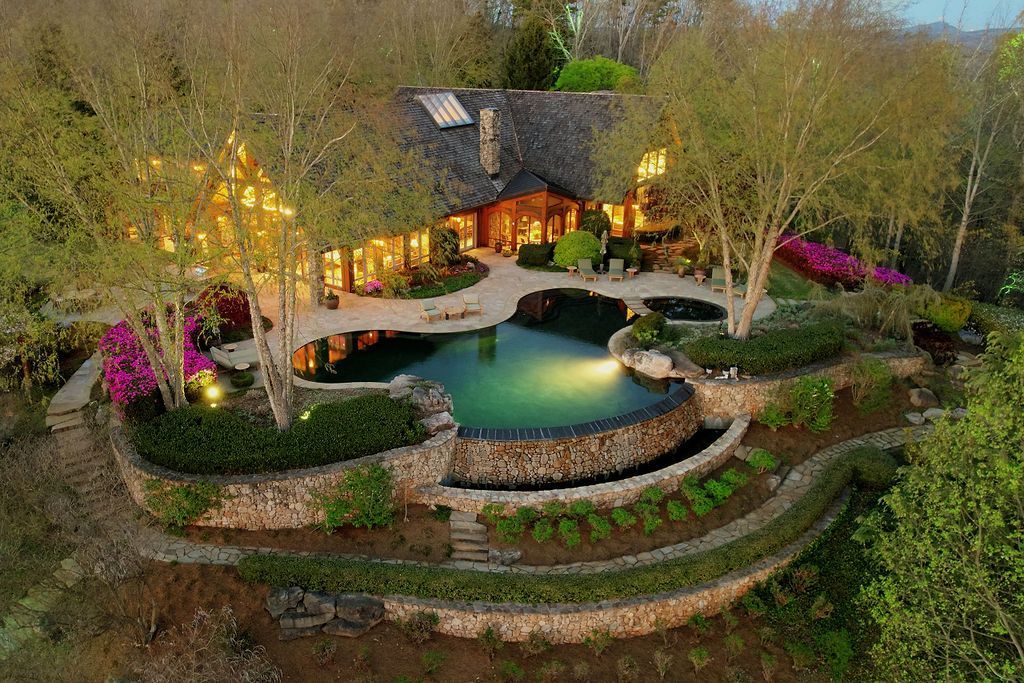 An aerial view of a large house with a swimming pool in the middle of a forest.
