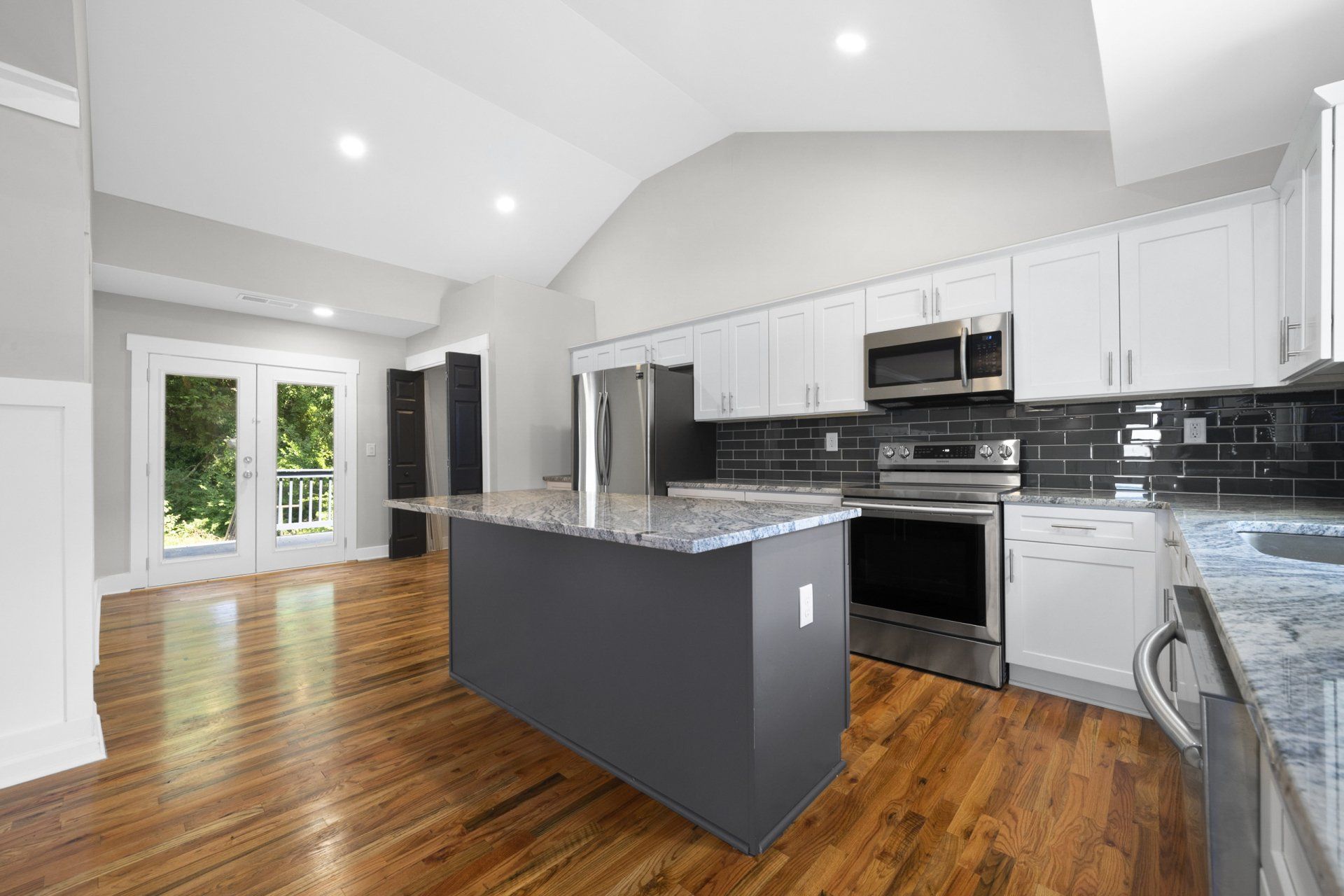 An empty kitchen with white cabinets , stainless steel appliances , granite counter tops and hardwood floors.