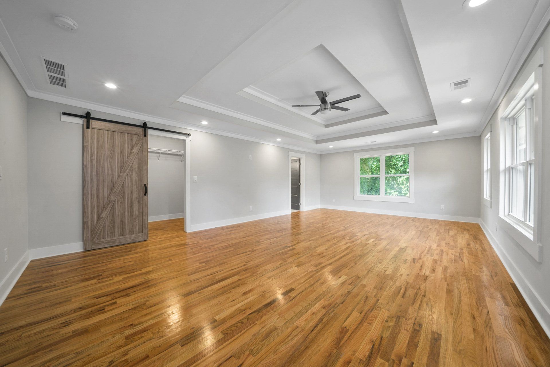 A large empty room with hardwood floors and a ceiling fan.