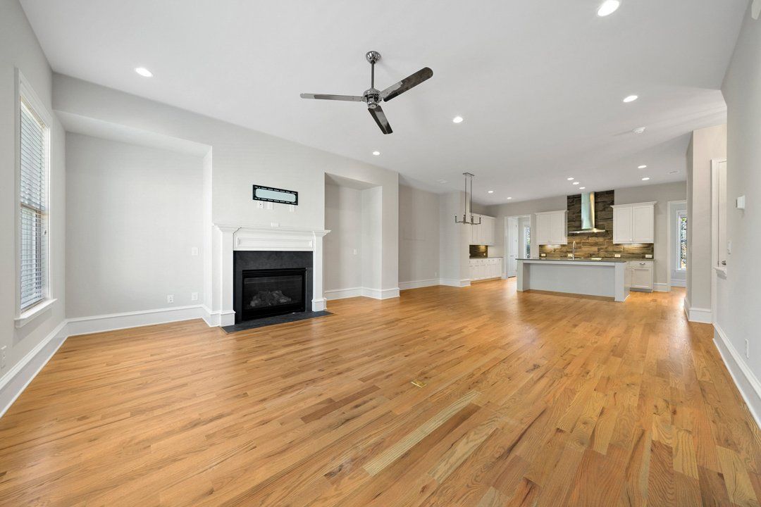 An empty living room with hardwood floors , a fireplace and a ceiling fan.