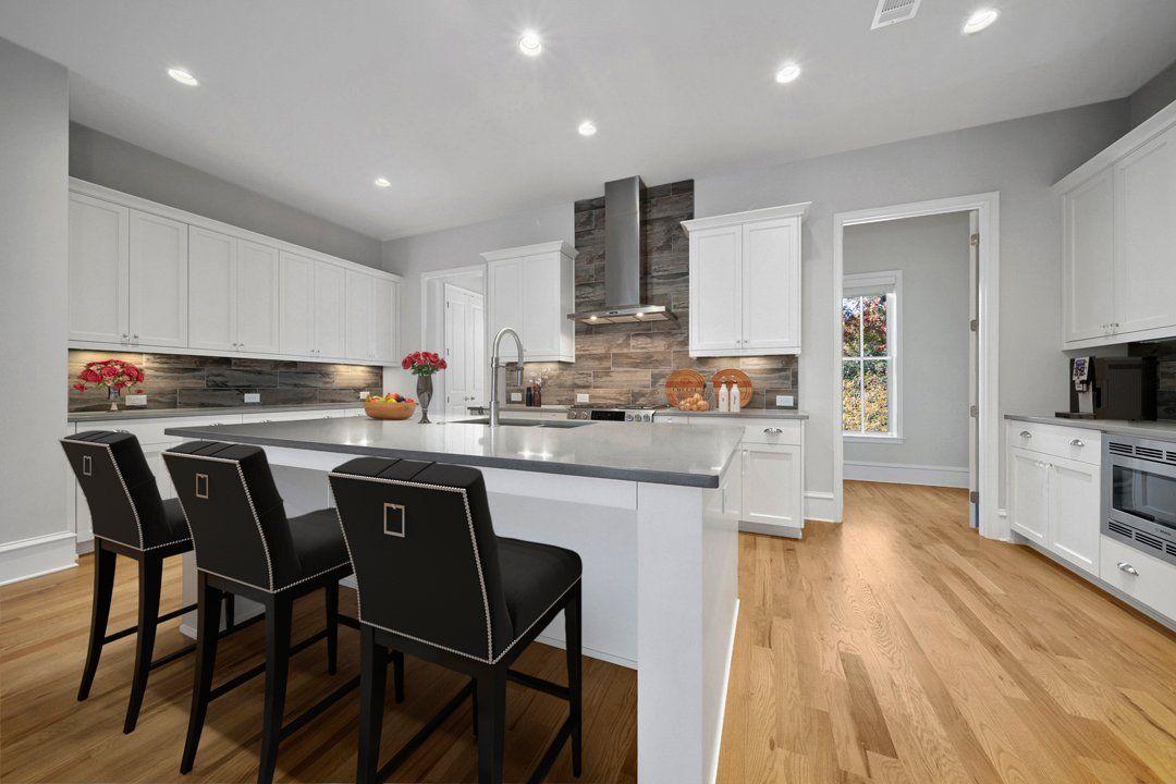 A kitchen with white cabinets , hardwood floors , and a large island.