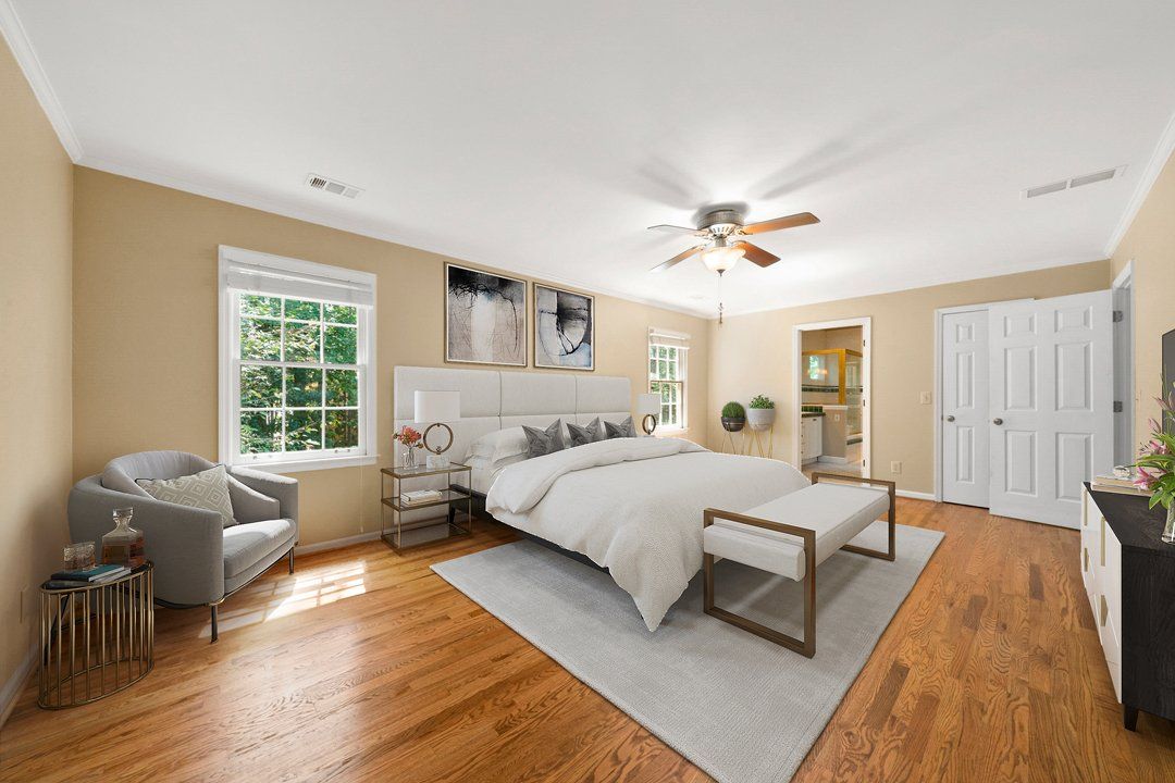 A bedroom with hardwood floors , a king size bed , a chair and a ceiling fan.