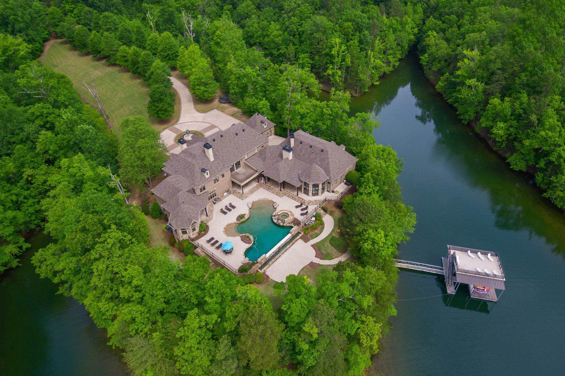 An aerial view of a large house on a small island in the middle of a lake surrounded by trees.